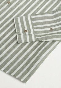 Gros plan du poignet d'une chemise à manches longues rayée verticalement vert et blanc avec des boutons marron sur fond blanc.