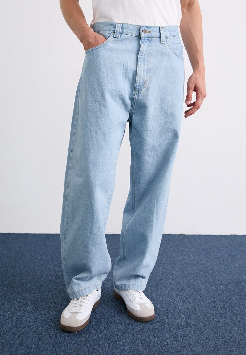 Helle blaue Jeans mit lockerem Schnitt, ausgestattet mit einem klassischen Knopfverschluss und fünf Taschen. Kombiniert mit weißen Turnschuhen.