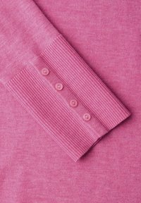 Poignet de pull en tricot rose avec une texture lisse et cinq boutons roses sur une bordure côtelée. Tissu doux et léger avec une couleur uniforme.