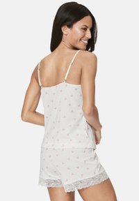 Weißes Schlafanzugset bestehend aus einem Tanktop und Shorts, verziert mit rosa Herzmustern und Spitzeneinfassung am Saum. Verstellbare Träger.