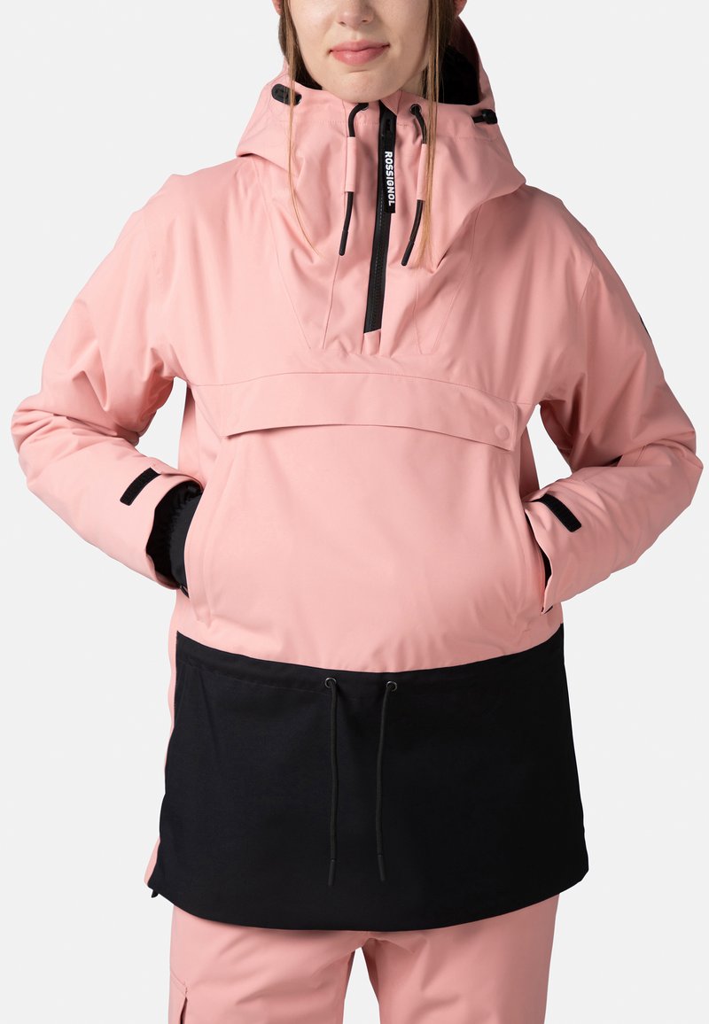 Rosa vattentät anorakjacka med en svart nederdel, har en justerbar huva, framficka och elastiska ärmslut. Slät textur.