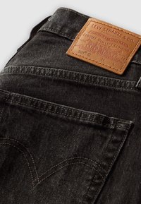 Jean Levi's 501 noir montrant la poche arrière et une étiquette de marque en cuir marron cousue à la ceinture.