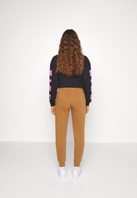 Svart sweatshirt med rosa tryck på ärmarna, kombinerad med bruna joggers och vita skor. Modellen ses bakifrån, med lockigt hår.