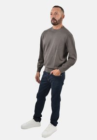 Maglione grigio leggero con polsini a costine, abbinato a jeans blu scuro e sneakers bianche. L'insieme presenta una vestibilità casual.