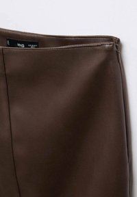 Jupe en simili cuir marron avec texture lisse. Elle présente une fermeture éclair cachée et une taille repliée avec un détail de couture sur le côté.