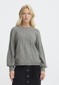 Maglione grigio chiaro lavorato a maglia con un motivo a costine testurizzato, maniche larghe e scollatura tonda, abbinato a una gonna in velluto a coste nera.