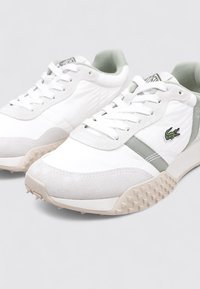 Zapatillas blancas con detalles en ante gris, suela de goma texturizada, diseño con cordones y el logo de Lacoste en verde en el lateral.