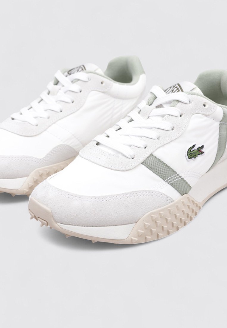 Zapatillas blancas con detalles en ante gris, suela de goma texturizada, diseño con cordones y el logo de Lacoste en verde en el lateral.