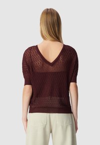 Bordeauxgebreide trui met een V-rug, voorzien van een diamantpatroon en korte mouwen. De stof lijkt semi-doorzichtig en lichtgewicht te zijn.