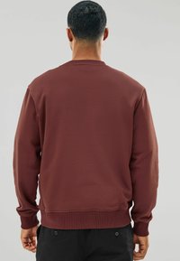 Sweatshirt vișiniu cu decolteu rotund, manșete și talie dintr-un material ribbonat. Realizat dintr-o țesătură moale, are o croială clasică. Fără logo-uri sau modele vizibile.