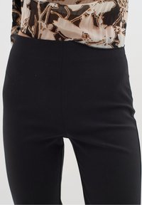 Zwarte broek van een gladde, rekbare stof; hoog in de taille; subtiele glans; geen zichtbare sluitingen of zakken; figuurvormige pasvorm.