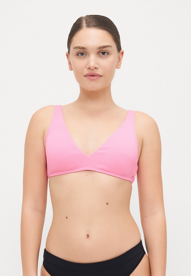 Rózsaszín bordázott bikini felsőrész V-kivágással és széles pántokkal. Simává textúrája és kontrasztos szélén kivitelezés jellemzi. A modellen fekete bikini alsó rész látható.