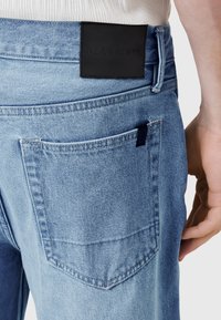 Svetlo modre jeans hlače iz jeansa s črnim usnjenim usnjenim obližem "ALLSAINTS" na pasu. Poudarjene klasične zadnje žepe in subtilni šivi.