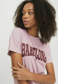 T-shirt di cotone rosa chiaro con il bold "BARCELONA" in burgundy stampato sul petto. Maniche corte e collo rotondo. Texture liscia.