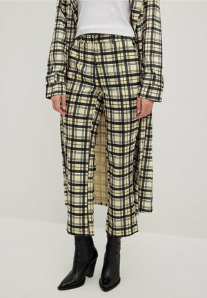 Pantalon à carreaux en crème et noir, avec une coupe ample et une taille élastique, associé à de sleek bottes noires à talons.