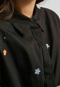 Czarna koszula z haftem kwiatowym w odcieniach pomarańczowym i niebieskim, z klasycznym kołnierzykiem i zapięciem na guziki, wykonana z gładkiego materiału.