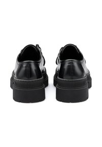 Scarpe in pelle verniciata nera con punta arrotondata, suola in gomma nera spessa e dettagli in tessuto sul retro. Finitura liscia con cuciture minime.