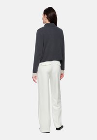 Graue verkürzte Jacke mit Kragen, kombiniert mit weißen, weit geschnittenen Hosen. Die Jacke hat eine strukturierte Stoffqualität und Spitzenakzente an den Ärmeln.