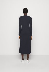 Marineblauwe jurk met lange mouwen, rechte pasvorm, ronde halslijn en lengte tot halverwege de kuit. Gemaakt van zachte, gestructureerde stof. Gecombineerd met witte schoenen.