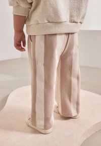 Pantalones a rayas beige y blancas con una textura suave, que cuentan con una cintura elástica y un ajuste relajado de pierna ancha, combinados con zapatillas blancas.