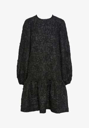 Svart kjole med teksturert, krøllete stoff. Har lange ermer og en sammenkrøllet volangkant. Rund hals, avslappet passform.