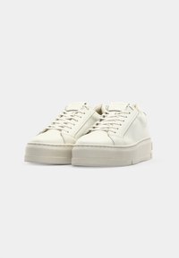 White leather sneakers with a rounded toe, flat sole, and tonal laces. Textured surface and minimalistic design with subtle stitching details.
