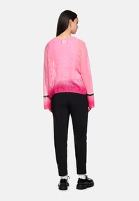 Rosa gradient Strickpullover mit langen Ärmeln, offener Struktur und schwarzen Streifenakzenten. Kombiniert mit schwarzen, schmal zulaufenden Hosen und klobigen Schuhen.