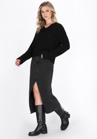 Czarny sweter prążkowany z dekoltem w serek, zestawiony z czarną maxi spódnicą dżinsową z rozcięciem z przodu oraz czarnymi botkami na obcasie z klamrami.