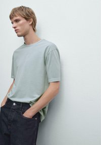 Light green short-sleeve t-shirt with a round neck, paired with black denim jeans. Soft fabric, relaxed fit, minimal stitching details.
