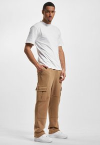 Pantalons cargo beiges avec plusieurs poches latérales, en tissu doux, associés à un t-shirt blanc simple et des baskets blanches.