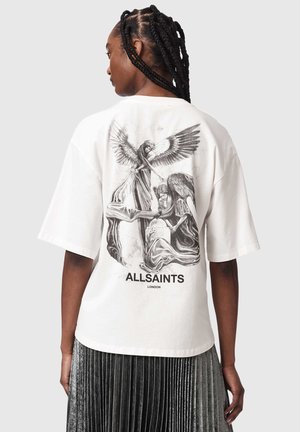 Person med flettet hår bærer en hvid oversized T-shirt med sort engleagtige figurer og teksten "ALLSAINTS LONDON" på ryggen.