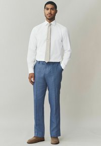 Pantaloni azzurri su misura abbinati a una camicia bianca e a una cravatta beige con motivi. Mocassini marroni completano l'outfit.