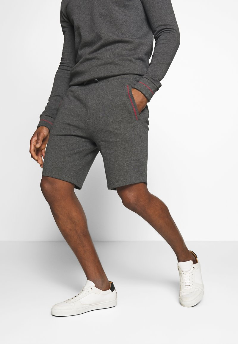 Shorts de sport gris en tissu doux, avec une coupe décontractée, des poches latérales avec des accents rouges, et associés à des baskets blanches.