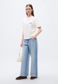 Λευκό βαμβακερό μπλουζάκι με μπλε λογότυπο "Calvin Klein", σε συνδυασμό με ανοιχτό μπλε τζιν παντελόνι φαρδιάς γραμμής και καφέ αθλητικά παπούτσια. Αξεσουάρ: μικρή κρεμ τσάντα χειρός.