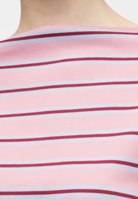 Κοντινό πλάνο από το πάνω μέρος της πλάτης ενός ατόμου που φοράει ροζ μπλούζα με οριζόντιες κόκκινες και γαλάζιες ρίγες.