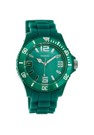 Montre avec un bracelet en silicone vert, un cadran rond, des aiguilles métalliques et de grands index. Elle est dotée d'un verre minéral et d'une lunette tournante.