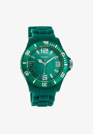 Montre avec un bracelet en silicone vert, un cadran rond, des aiguilles métalliques et de grands index. Elle est dotée d'un verre minéral et d'une lunette tournante.
