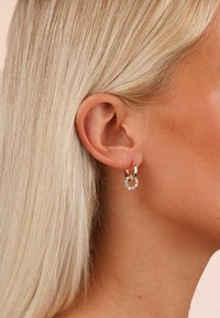 Guldörhängen i form av hoop med en mindre cirkulär accent, prydd med klara kristaller. Designen har en slät, glänsande yta.