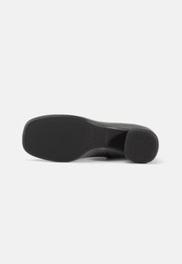 Suela de zapato negra con punta cuadrada y tacón cuadrado, que muestra un patrón de agarre texturizado en la suela y en la parte inferior del tacón.