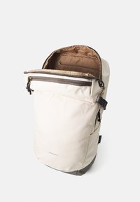 Lys beige ryggsekk med roll-top design og brun innside. Har en glidelommer og justerbare stropper. Solid materiale.