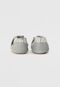 Zapatos de cuero gris con un detalle trasero a rayas azules y blancas, que presentan una textura suave y un diseño de punta redondeada.
