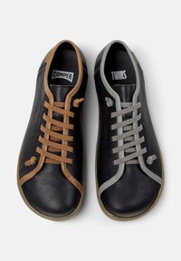 Scarpe in pelle nere con lacci a contrasto: un lato presenta lacci marroni con l'etichetta "CAMPER," mentre l'altro lato ha lacci grigi con l'etichetta "TWINS."