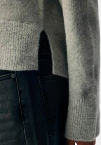 Grå stickad tröja med ribbad textur, sidoklipp och en mjuk, lurvig finish, buren över mörka denimjeans med synlig sömnad.