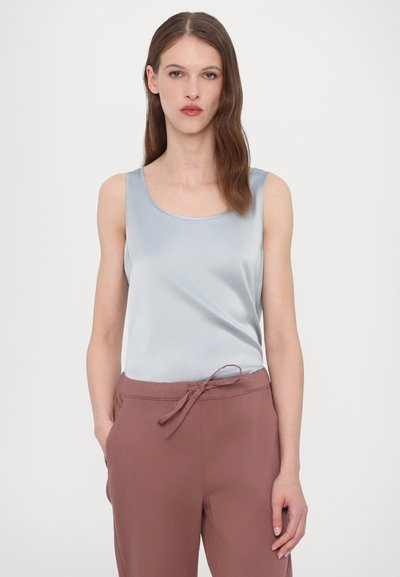 Jasnoniebieski satynowy top na ramiączkach z okrągłym dekoltem, zestawiony z miękkimi brązowymi spodniami na sznurek. Tkanina wydaje się gładka i refleksyjna.