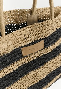Vävd halm tote-väska med beige och svarta ränder, naturlig fibertyp, förstärkta handtag och en läderpatch med varumärkesnamn.