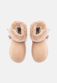 Botas de ante falso en tono marrón claro con un suave puño de pelo sintético beige y un detalle de lazada en la parte trasera. Punta redondeada y suela plana.