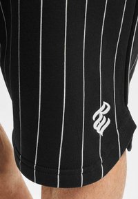 Șorturi tricotate negre cu dungi verticale subțiri albe, având un mic logo brodat pe tiv și o textură moale.
