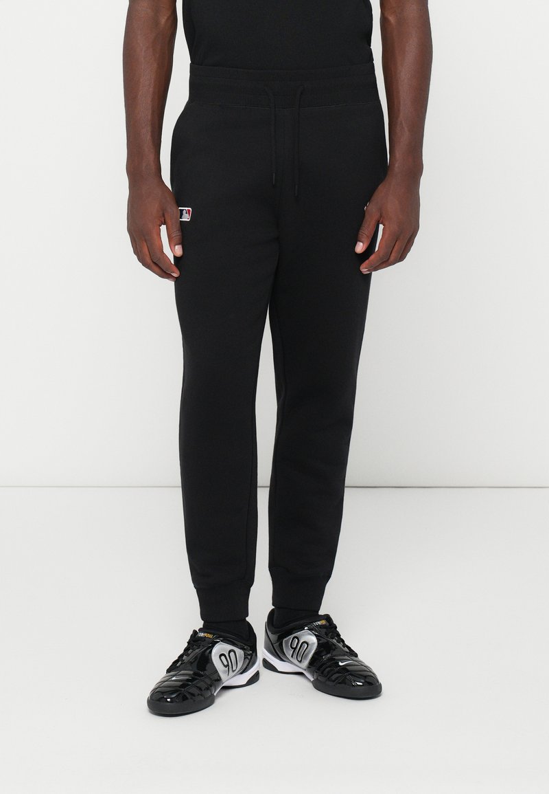 Pantaloni de trening negri dintr-un material cu textură netedă, având un talie elastică și tivuri la gleznă. Detaliu subtil cu logo pe lateral.