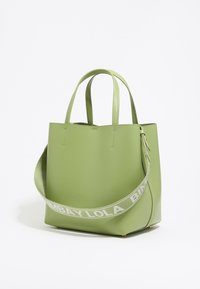 Green faux leather tote bag with two top handles and a removable shoulder strap featuring white branded text. Smooth texture and minimalist design.