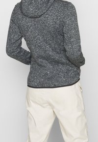 Szary dziany hoodie o teksturowanym wykończeniu, dopasowany krój i czarny dół. Noszony z jasnymi, luźnymi spodniami.